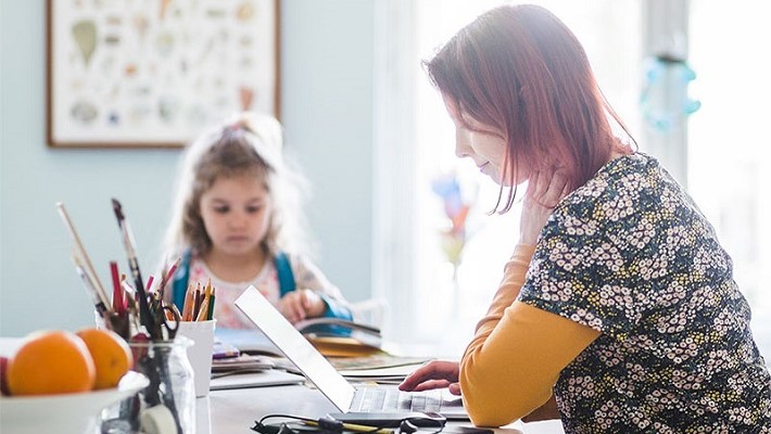 Side view of adult working on laptop while sitting with child at kitchen island