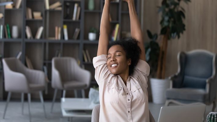 Woman stretching overhead while working remotely on her laptop