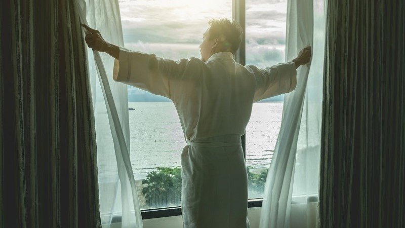 man opening the curtains with a sea view