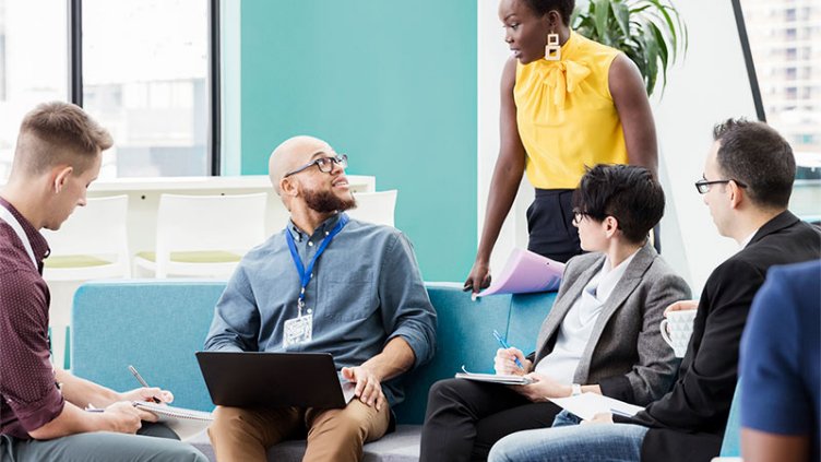 People working in an office sitting on couches, working on their devices