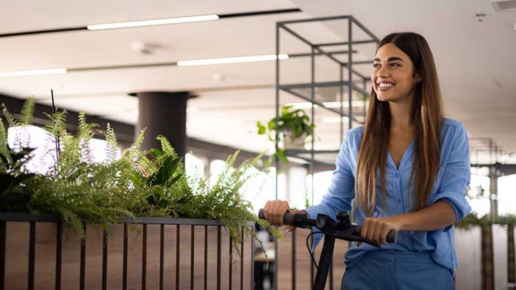 Happy businesswoman leaving the office with a push scooter