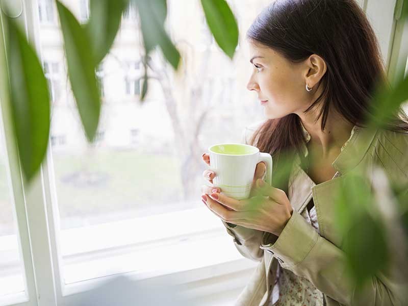 A woman enjoying her coffee while looking at the garden area inside the office
