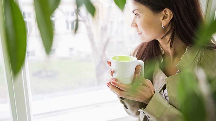 A woman enjoying her coffee while looking at the garden area inside the office