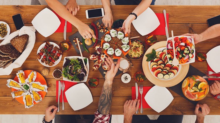 People eat healthy meals at festive table served for party. Friends celebrate with organic food on wooden table top view. Happy company having lunch, taking sandwiches from dish