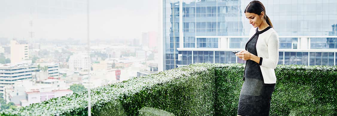 Smiling female business executive standing on office terrace looking at information on smartphone